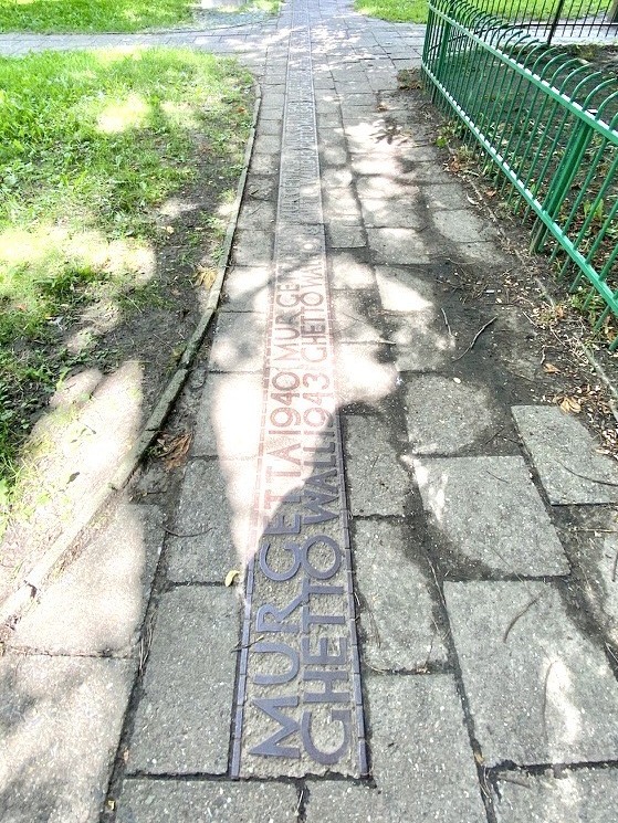 Memorial marker embedded in the Warsaw sidewalk reading MUR GETTA 1940 GHETTO WALL 1943, tracing the former line of the Jewish Ghetto wall.